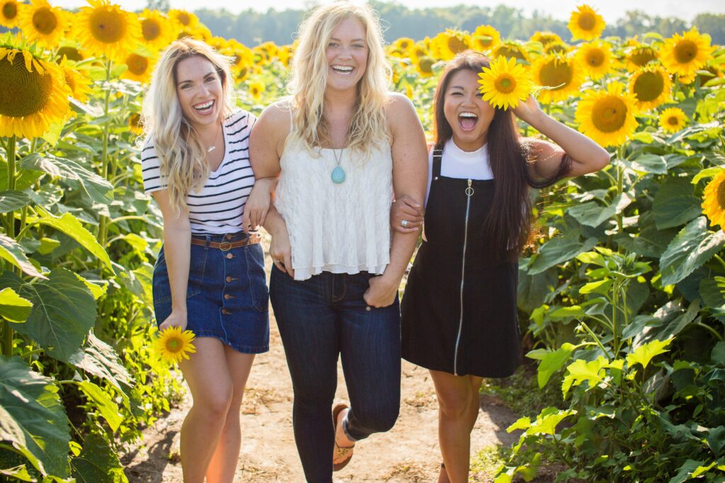 Three women laughing and enjoying the vibrant sunflower fields near Chateau Charente, embracing the joy of nature and companionship during an art retreat.